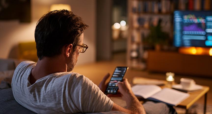 Homem estudando criptomoedas em casa com material educativo e celular.